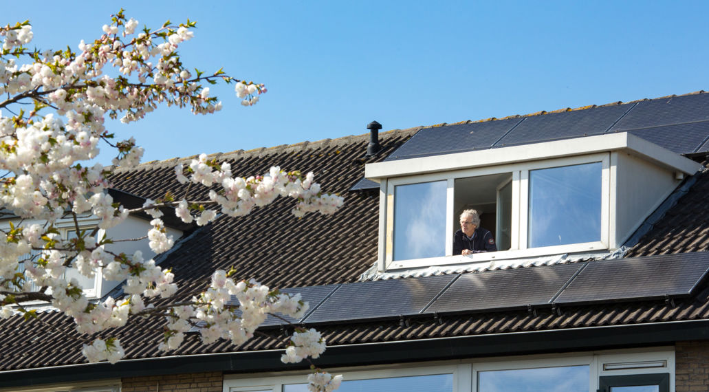 Een man kijkt uit zijn dakraam. Op het dak liggen zonnepanelen.